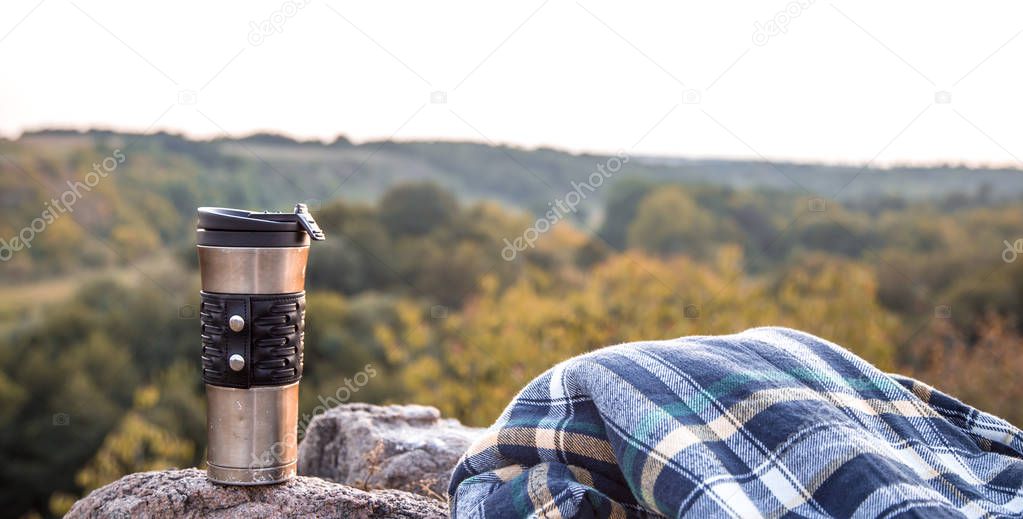 camping items, thermos with jacket on a stone on the background of nature, the concept of travel and recreation