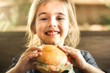Bir kafede bir çocuk fast food yemek kavramı bir sandviç yeme küçük şirin kız