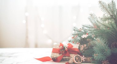 Noel coziness ışıkları ve bir Noel ağacı ve tablo, metin için yer kırmızı fiyonklu bir hediye dalları ile hafif bir arka plan üzerinde bir odada