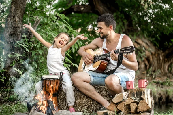 Dad\'s family camping plays guitar to his daughter in nature, the concept of family values and pastime