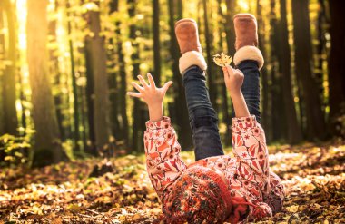 Güneş ışığı altında vakit çocuklu autumn kavramı yerde yatan küçük kız sonbahar üzerinde oynamaya kalkıyor