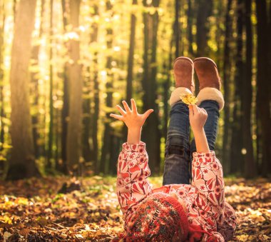 Güneş ışığı altında vakit çocuklu autumn kavramı yerde yatan küçük kız sonbahar üzerinde oynamaya kalkıyor