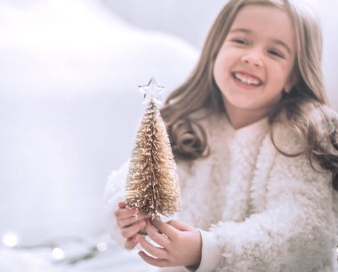 Sevimli küçük bir kız ve bir kız hafif bir arka plan üzerinde elinde güzel bir küçük ağaç Noel arka plan