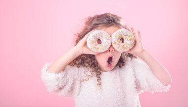 Kıvırcık saçlı ve onun elinde iki ağız sulandıran donut biraz şaşırmış bir kız portresi donuts, pembe bir arka plan üzerinde gözleriyle kapatır