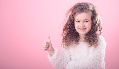 Pembe bir arka plan üzerinde yukarıyı kıvırcık saçlı sevimli küçük gülümseyen kız portresi