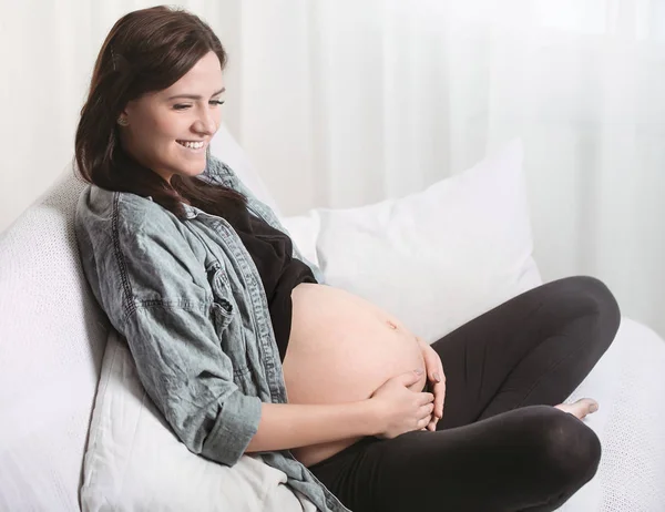 年轻美丽的孕妇坐在窗边的沙发上 怀孕的概念和对孩子的期待 — 图库照片