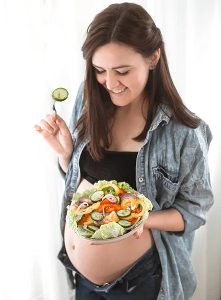 年轻孕妇在家里吃蔬菜沙拉附近的窗口 怀孕和健康饮食的概念 — 图库照片