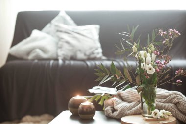 Rahat ev iç dekorasyonu ile siyah bir kanepe oturma odasında unsurları ve bir vazo çiçek ve küçük bir tablo üzerinde yanan mumlar