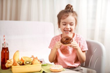 Küçük güzel neşeli kız meyve evde masada, Çocuk gıda kavramı ile bir çörek ve öğle yemeği kutusu yeme