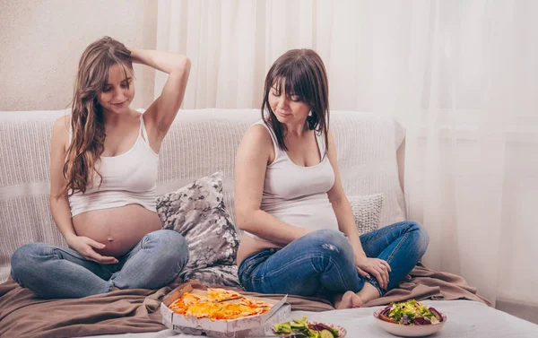 产妇概念 两个孕妇吃比萨饼和沙拉在家里的沙发 友谊和健康的饮食 — 图库照片