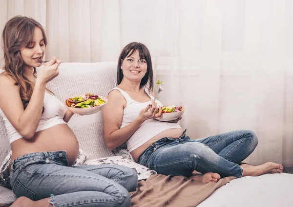 产妇的概念 两个孕妇吃新鲜沙拉在家里的沙发上 友谊和健康的饮食 — 图库照片
