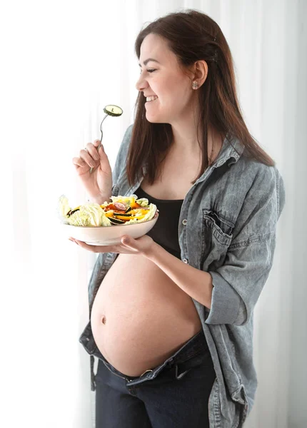 年轻孕妇在家里吃蔬菜沙拉附近的窗口 怀孕和健康饮食的概念 — 图库照片