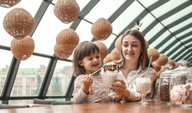 Masada oturan ve bir milkshake bir restoran veya Cafe içme çocuk mutlu genç kadınlar anne. Boş zaman ve çocuk restoran ile iletişim içinde. Aile kavramı