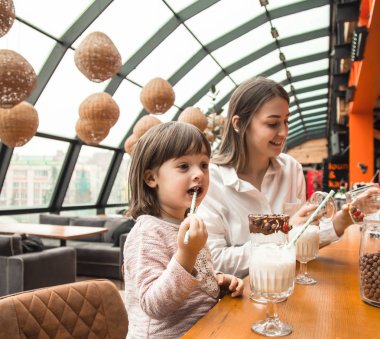 Masada oturan ve bir milkshake bir restoran veya Cafe içme çocuk mutlu genç kadınlar anne. Boş zaman ve çocuk restoran ile iletişim içinde. Aile kavramı