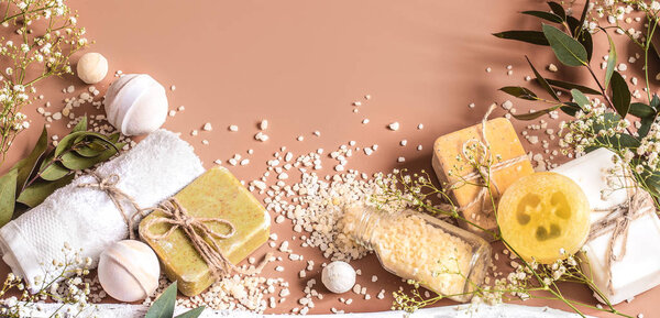 Spa concept with towels, soap, salt, leaves, flowers, bath bombs and body and face accessories on colored background. Place for text