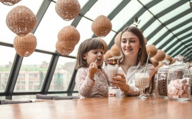 Masada oturan ve bir milkshake bir restoran veya Cafe içme çocuk mutlu genç kadınlar anne. Boş zaman ve çocuk restoran ile iletişim içinde. Aile kavramı