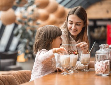Masada oturan ve bir milkshake bir restoran veya Cafe içme çocuk mutlu genç kadınlar anne. Boş zaman ve çocuk restoran ile iletişim içinde. Aile kavramı