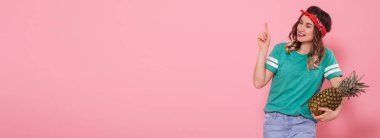 İçinde yeşil t-shirt ananas ile el gülümseyen güzel genç kız parmak pembe arka plan gösterir. Metin için yer.