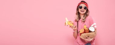 Pembe tişört ve gözlük, güzel genç kız seksi muz ve meyve dolu çanta pembe arka plan üzerinde tutarak. Yaz ve dinlenme. Metin için yer. Reklam kavramı