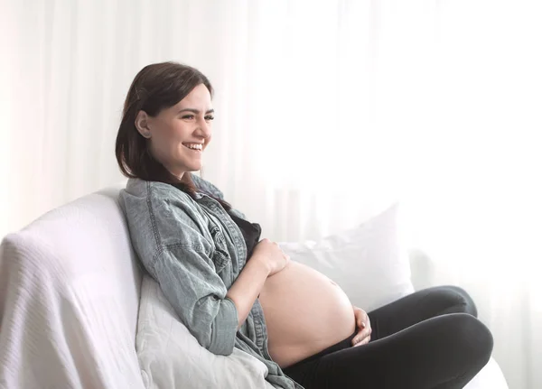 年轻美丽的孕妇坐在窗边的沙发上 怀孕的概念和对孩子的期待 — 图库照片