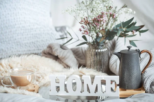 Home spring still life with a cup of coffee and a teapot on the background of the bed and a wooden inscription home