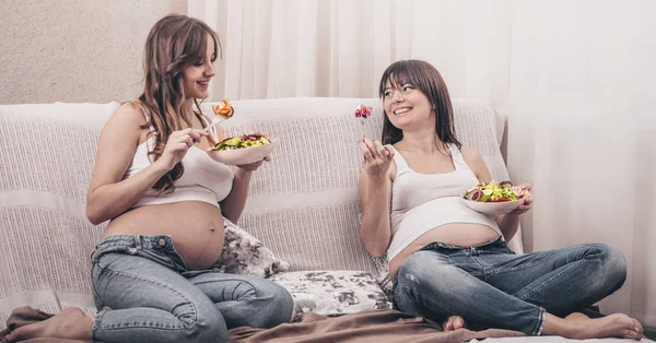 产妇的概念 两个孕妇吃新鲜沙拉在家里的沙发上 友谊和健康的饮食 — 图库照片