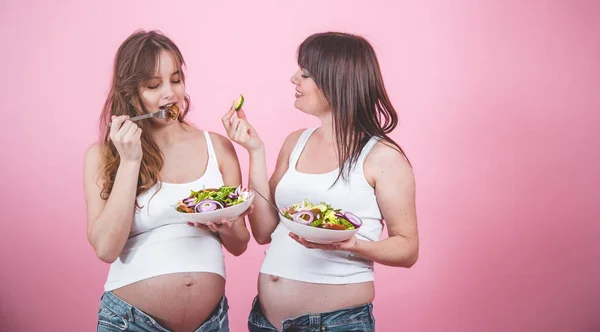 产妇概念 两个孕妇吃新鲜沙拉粉红色的背景 牛仔裤和白色 女性友谊 — 图库照片