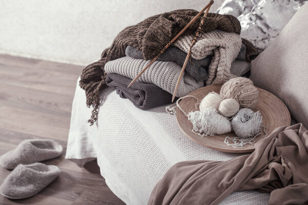 Vintage wooden knitting needles and threads on a cozy sofa with pillows and Slippers nearby. Still life photo. The concept of comfort