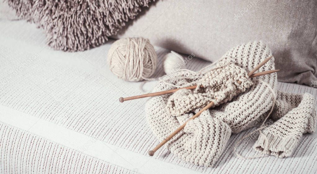 Vintage wooden knitting needles and threads for knitting on a cozy sofa with pillows and sweaters. Still life photo. The concept of comfort