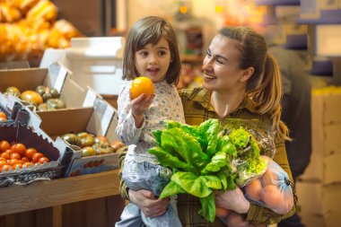 Süpermarkette bir aile. Güzel genç anne ve küçük kızı gülümseyip yiyecek alıyorlar. Sağlıklı beslenme kavramı. Hasat et