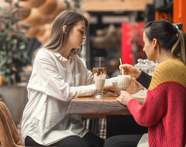 Dos mujeres felices están sentadas en un café, bebiendo batidos. , — Foto de Stock