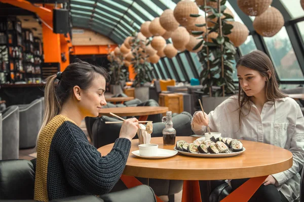 Dos mujeres felices sentadas en un café, comiendo sushi — Foto de Stock
