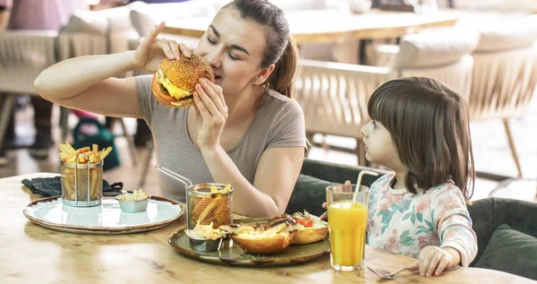 Mamá con una linda hija comiendo comida rápida en un café — Foto de Stock