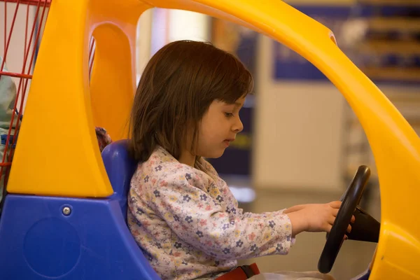 Linda niña en el pequeño carro de juguete en el supermercado — Foto de Stock