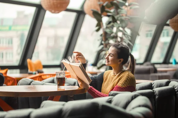 Joven hermosa mujer en suéter naranja lectura libro interesante en la cafetería — Foto de Stock