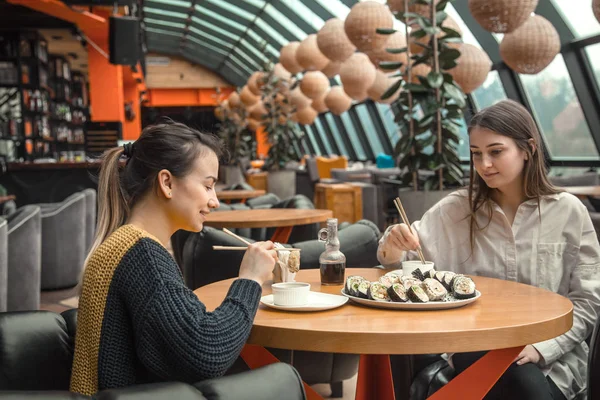 Dos mujeres felices sentadas en un café, comiendo sushi — Foto de Stock