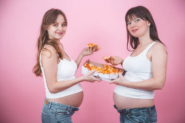 Concetto di nutrizione, donne incinte che mangiano pizza su sfondo rosa — Foto Stock
