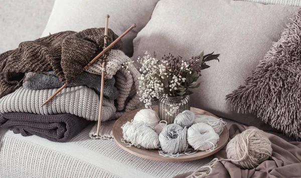 Ferri da maglia in legno vintage e fili su un accogliente divano con cuscini e un vaso di fiori — Foto Stock
