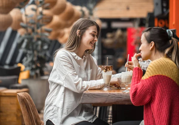 Dos mujeres felices están sentadas en un café, bebiendo batidos. , — Foto de Stock