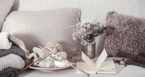 Vintage trä stickning nålar och trådar på en mysig soffa med kuddar och en vas med blommor. Öppen bok för läsning — Stockfoto