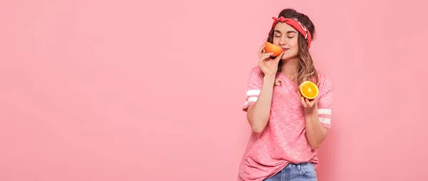Красивая молодая девушка в розовой футболке, держит смешной сексуальный оранжевый на розовом фоне. Лето и отдых — стоковое фото