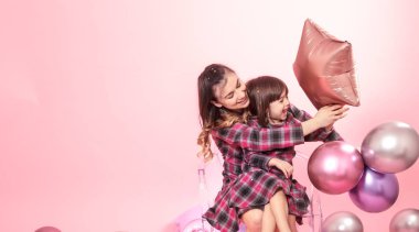 Komik anne ve bir şık sandalye pembe şeffaf arka plan üzerinde oturan çocuk. Küçük kız ve annesi balonlar ve konfeti ile eğleniyor