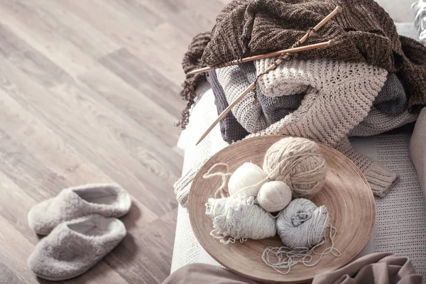 Ferri da maglia in legno vintage e fili su un accogliente divano con cuscini e pantofole nelle vicinanze — Foto Stock