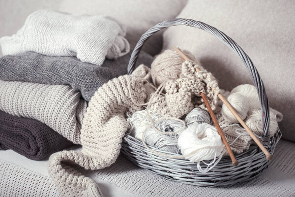 Vintage wooden knitting needles and threads in a large basket on a cozy sofa with sweaters. Still life photo