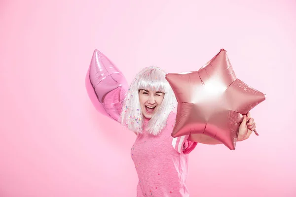 Смешная девушка с серебристыми волосами дает улыбку и эмоции на розовом фоне. Девушка или девушка-подросток с воздушными шарами и конфетти — стоковое фото