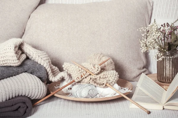 Vintage trä stickning nålar och trådar på en mysig soffa med kuddar och en vas med blommor. Öppen bok för läsning — Stockfoto