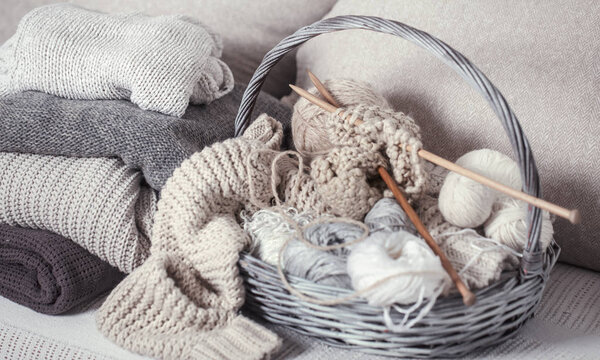 Vintage wooden knitting needles and threads in a large basket on a cozy sofa with sweaters. Still life photo