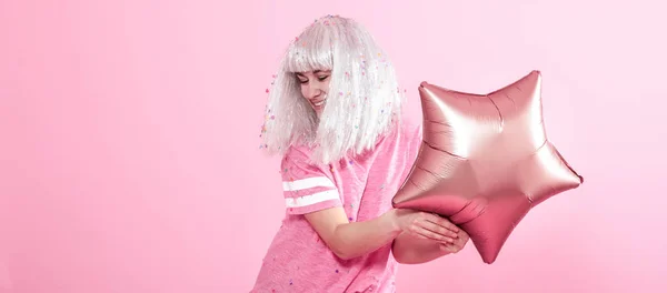 Funny Girl with silver hair gives a smile and emotion on pink background. Young woman or teen girl with balloons and confetti