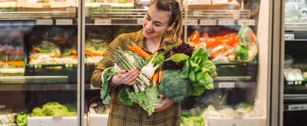 Woman in the supermarket. Beautiful young woman shopping in a supermarket and buying fresh organic vegetables