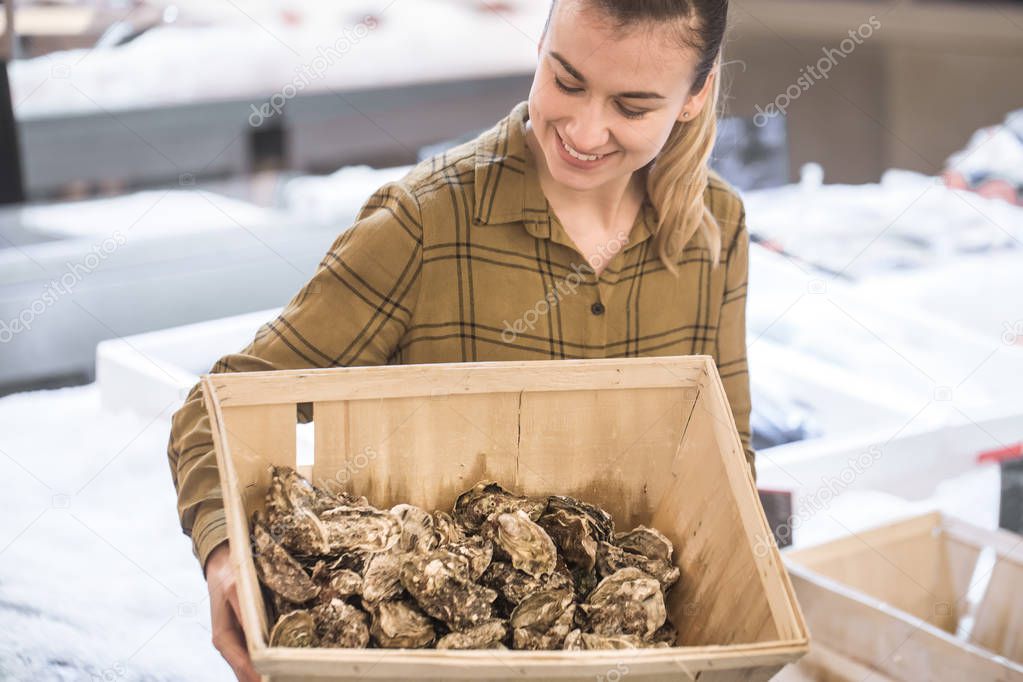 Woman in the supermarket with oysters. Beautiful young woman is holding a large box of oysters